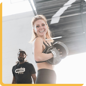 Image d’illustration : femme souriante tenant un haltère dans une salle de sport, posture motivée et dynamique.